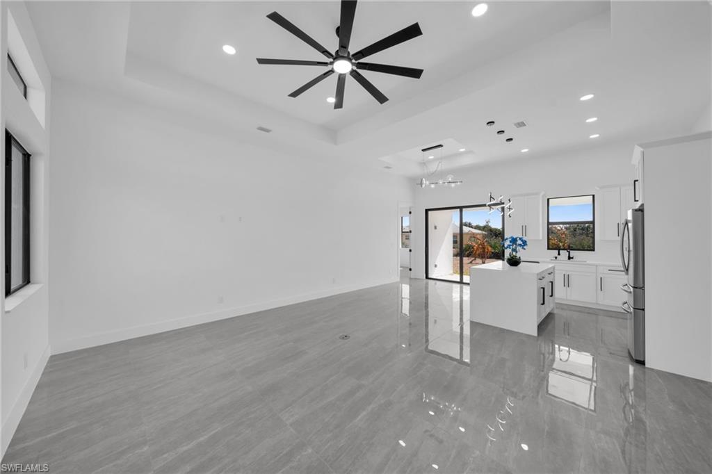 Unfurnished living room featuring a ceiling fan, a chandelier, and a tray ceiling