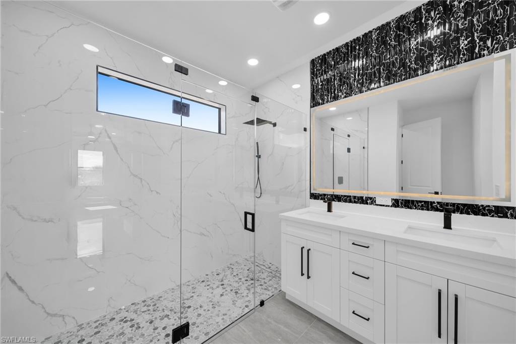 Bathroom featuring double vanity, a marble finish shower, and recessed lighting