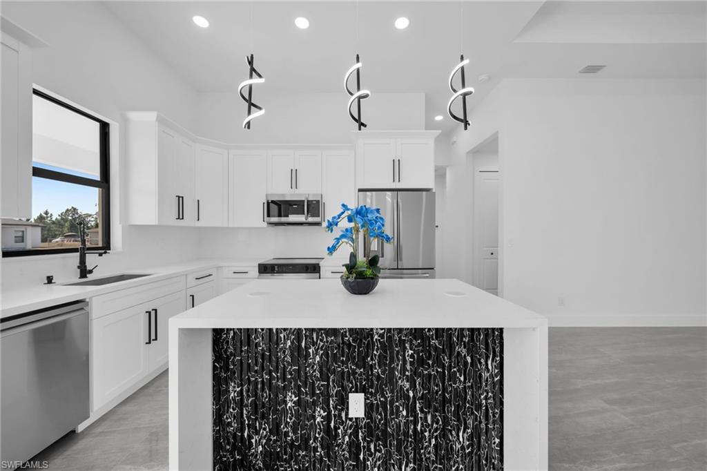 Kitchen with stainless steel appliances, light stone counters, white cabinets, and a center island