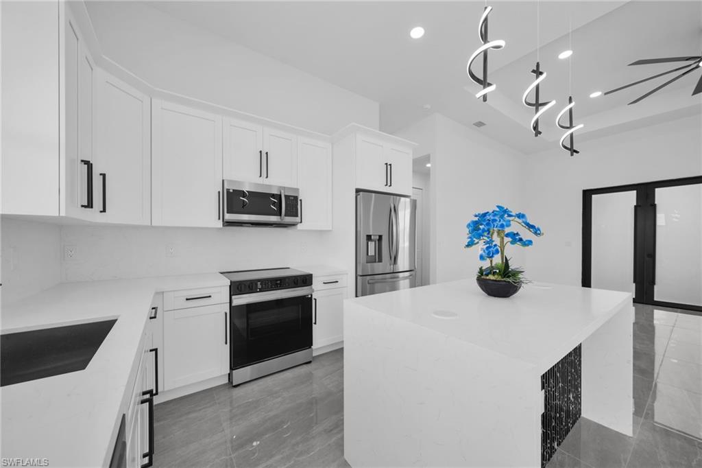 Kitchen with a kitchen island, light stone countertops, stainless steel appliances, and white cabinetry