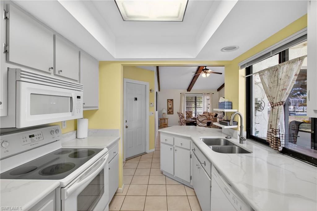 Kitchen featuring white appliances, light tile patterned flooring, a peninsula, white cabinetry, and a ceiling fan