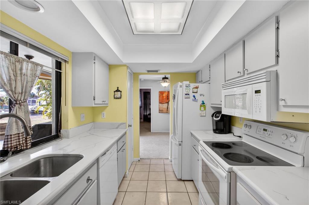 Kitchen with white appliances, white cabinets, a raised ceiling, light tile patterned floors, and light stone countertops