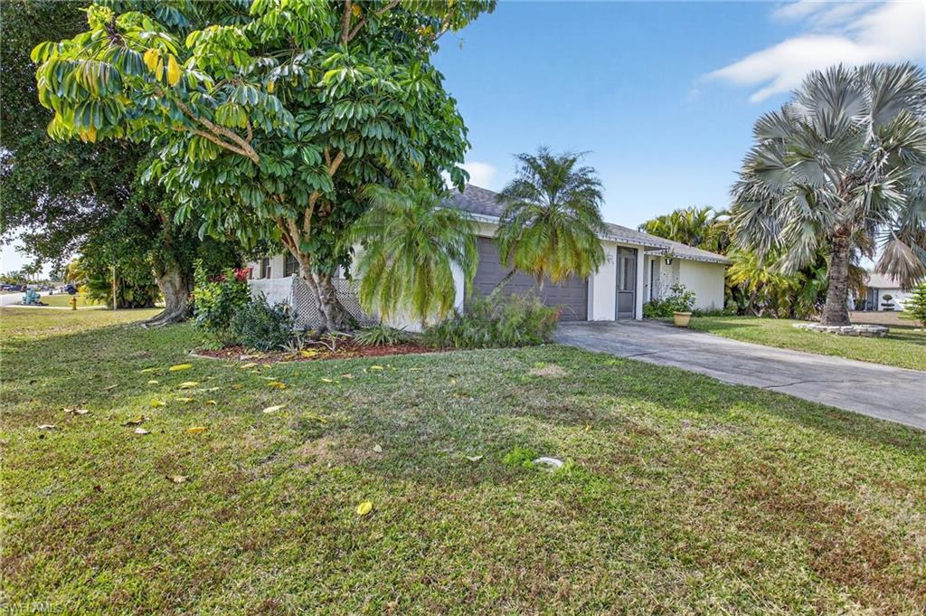 View of property hidden behind natural elements featuring concrete driveway, a front lawn, and an attached garage