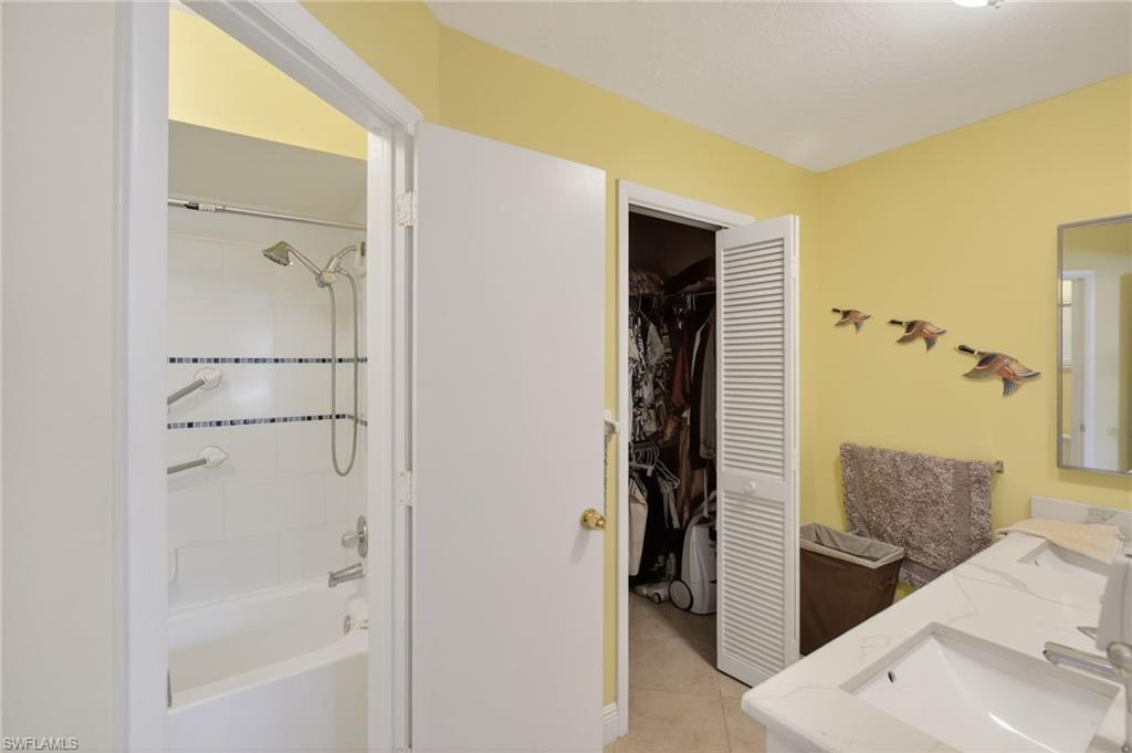 Bathroom featuring double vanity, shower / bath combination, light tile patterned floors, and a walk in closet