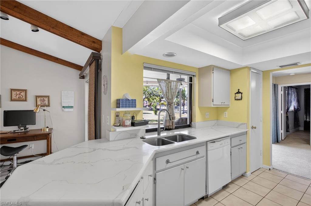 Kitchen featuring a peninsula, light colored carpet, dishwasher, light stone countertops, and white cabinetry