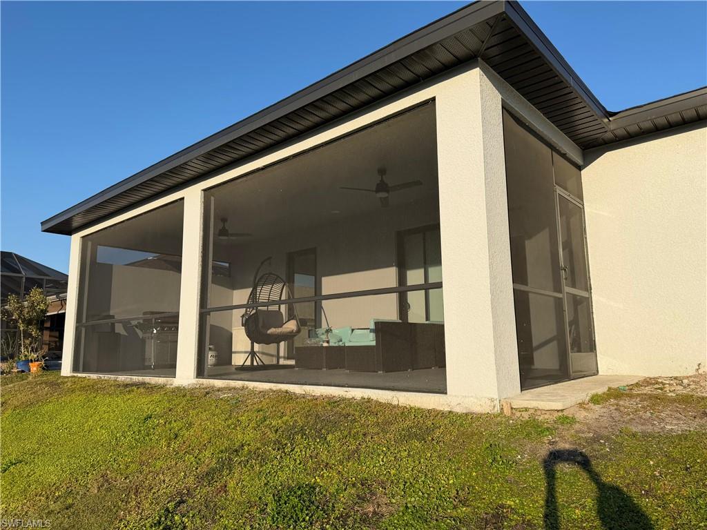 Back of house with a sunroom, stucco siding, and a lawn