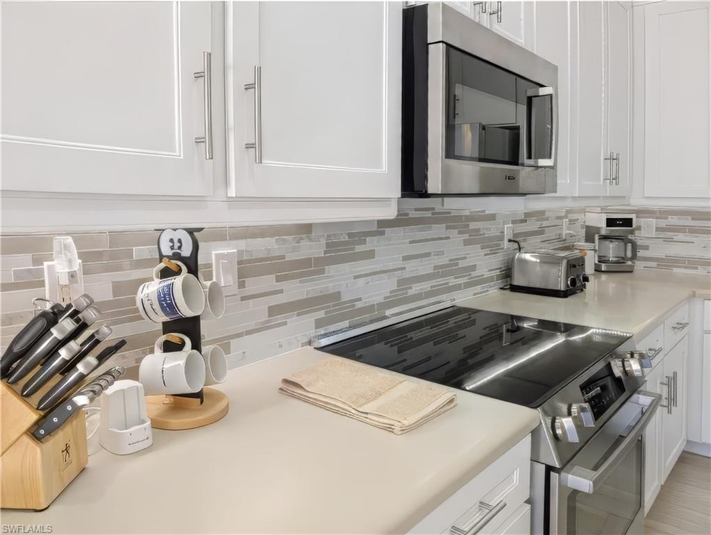 Kitchen with backsplash, white cabinets, and stainless steel appliances