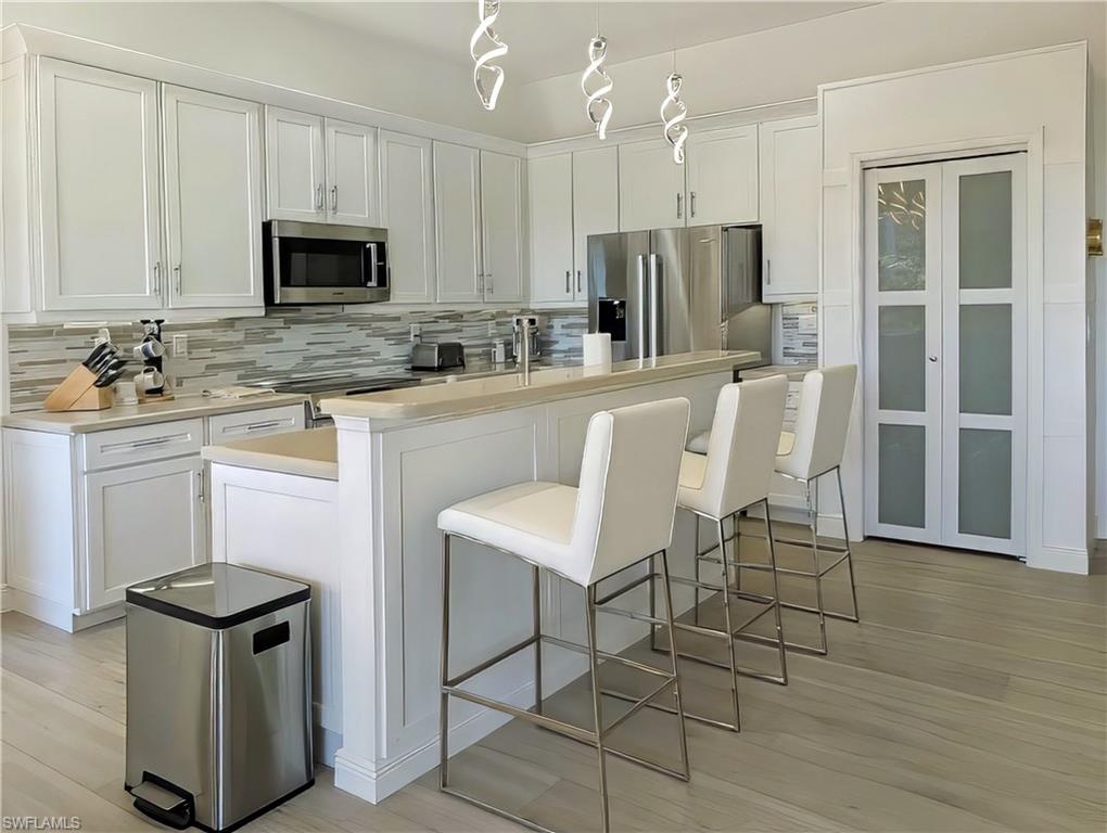 Kitchen with white cabinetry, decorative backsplash, a breakfast bar, a center island with sink, and appliances with stainless steel finishes