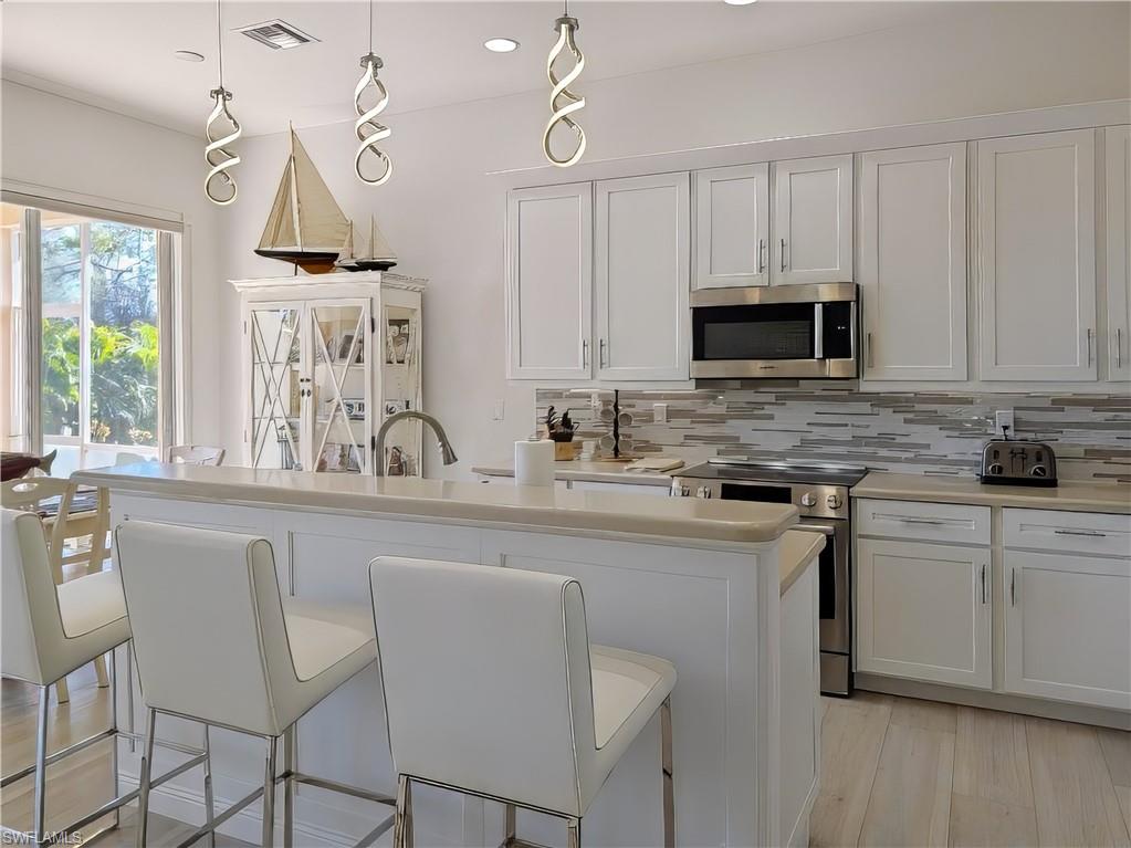 Kitchen with white cabinets, an island with sink, appliances with stainless steel finishes, decorative light fixtures, and a breakfast bar area