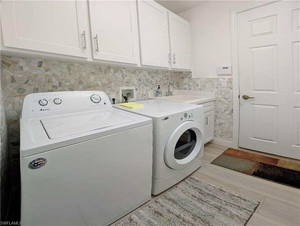 Clothes washing area featuring washer and dryer, light composite flooring, cabinets, and sink