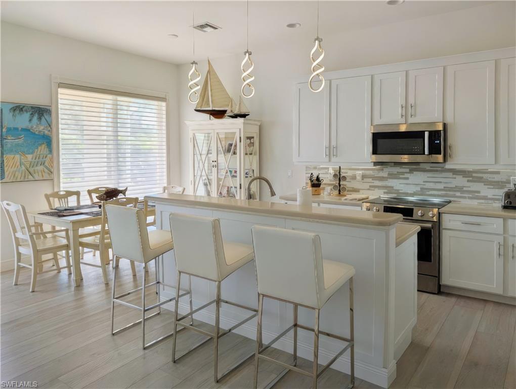 Kitchen with white cabinets, decorative light fixtures, stainless steel appliances, and an island with sink