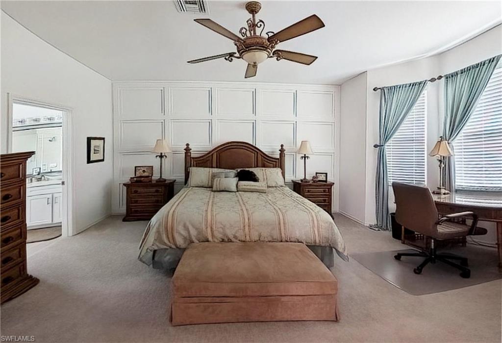 Carpeted bedroom with a ceiling fan, an office area, and a decorative wall