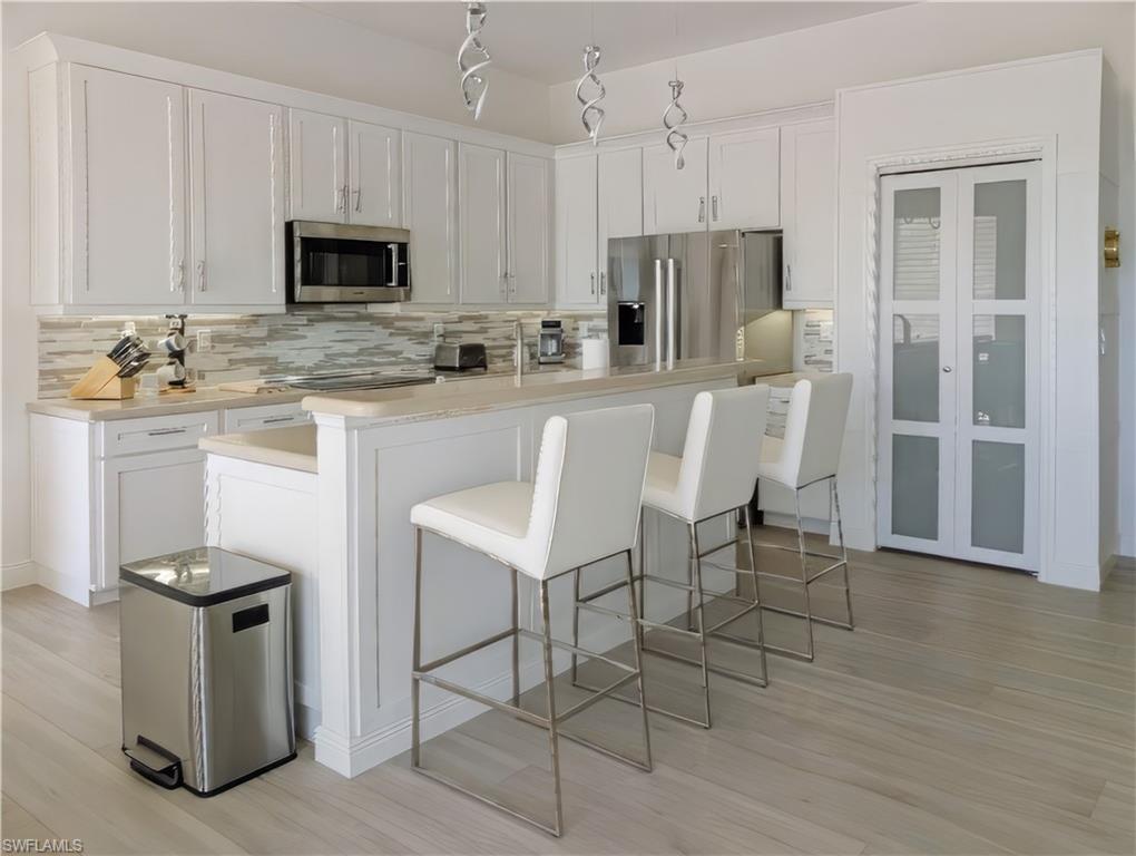 Kitchen featuring a kitchen breakfast bar, decorative backsplash, white cabinets, and stainless steel appliances