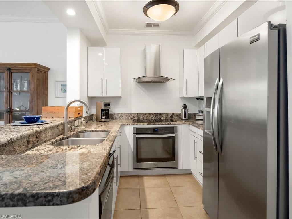 Kitchen featuring stainless steel appliances, range hood, dark stone counters, ornamental molding, and white cabinets