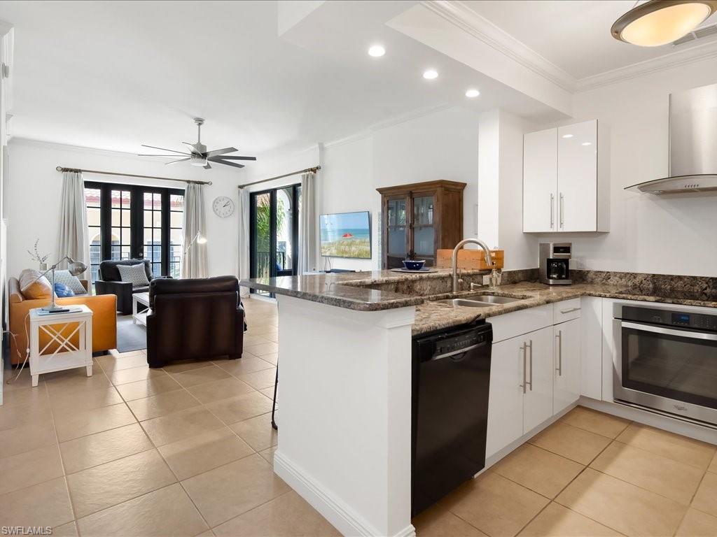Kitchen with ornamental molding, a peninsula, white cabinets, dark stone counters, and black appliances