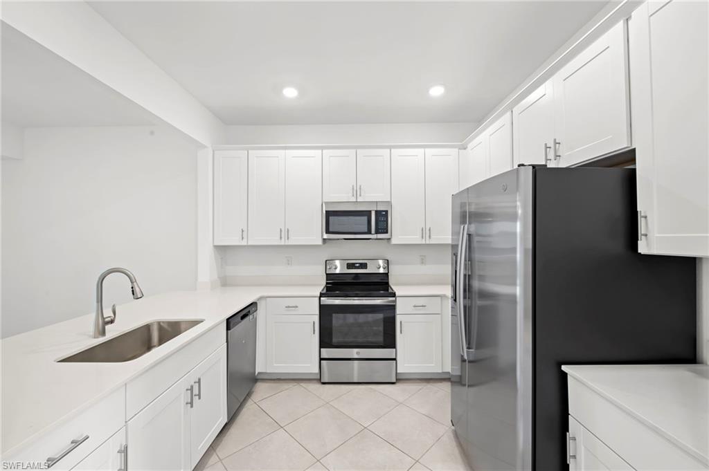 Kitchen with stainless steel appliances, white cabinets, light tile patterned floors, recessed lighting, and light stone countertops