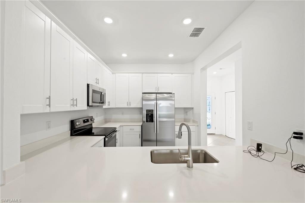 Kitchen with stainless steel appliances, white cabinetry, recessed lighting, light stone countertops, and a peninsula