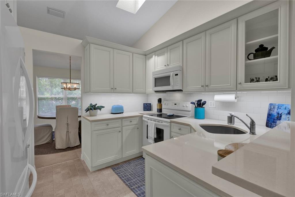 Kitchen featuring white appliances, vaulted ceiling, a skylight, light stone counters, and glass fronted cabinets