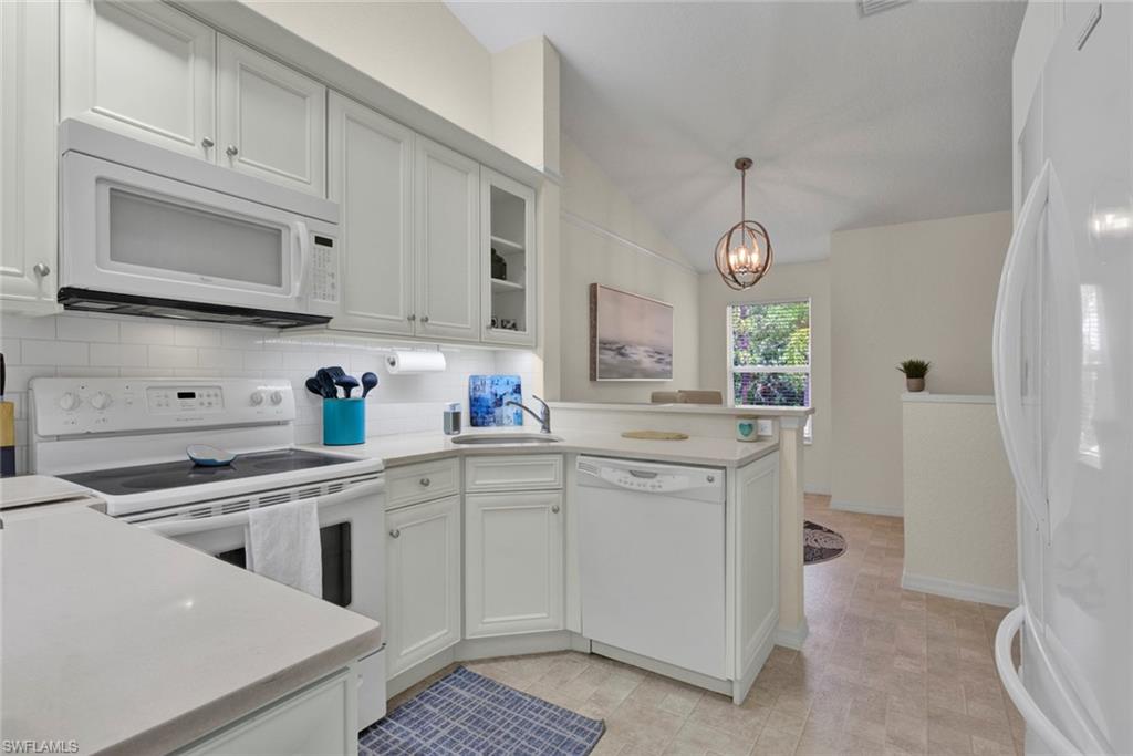 Kitchen with white appliances, tasteful backsplash, vaulted ceiling, hanging lights, and a peninsula