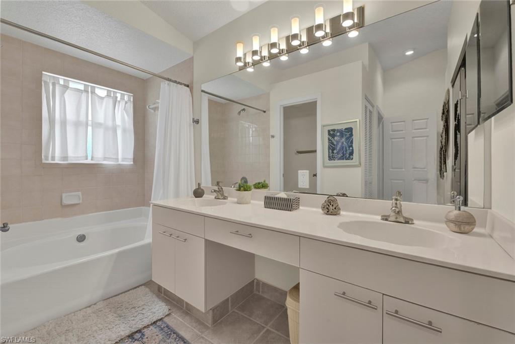 Bathroom featuring double vanity, shower / tub combo, and light tile patterned flooring