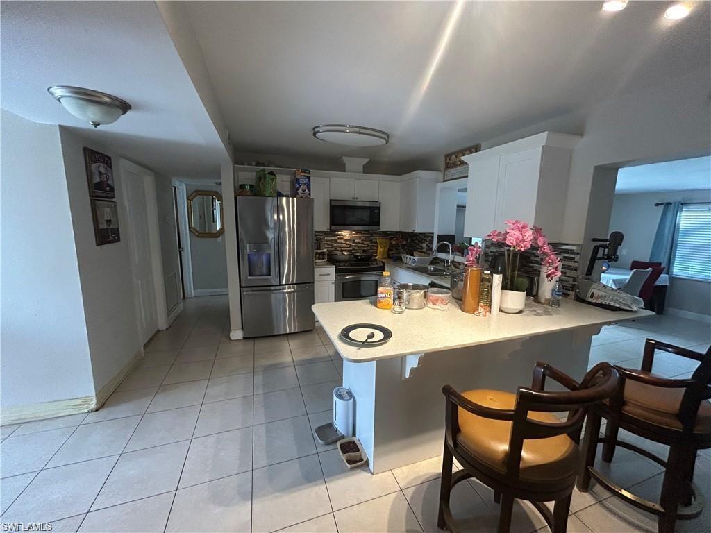 Kitchen featuring stainless steel appliances, decorative backsplash, white cabinets, and light tile patterned floors
