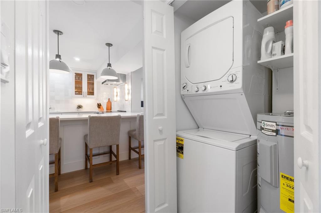 Laundry area with water heater, light wood-style flooring, and stacked washer and dryer