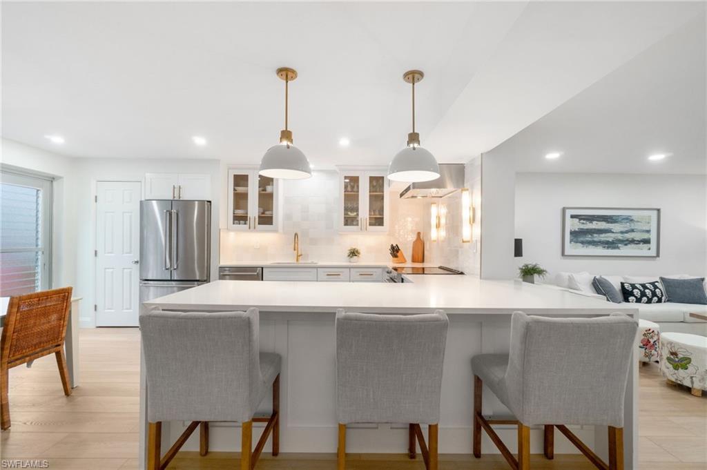 Kitchen featuring glass insert cabinets, a peninsula, pendant lighting, a breakfast bar area, and decorative backsplash