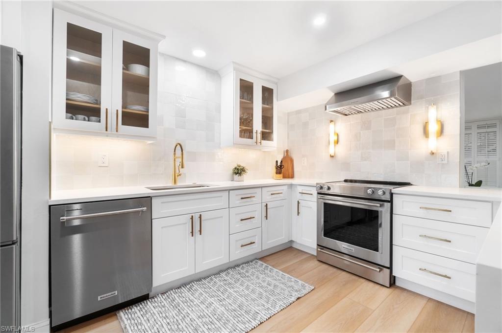 Kitchen with stainless steel appliances, white cabinetry, light stone countertops, backsplash, and light wood-style flooring