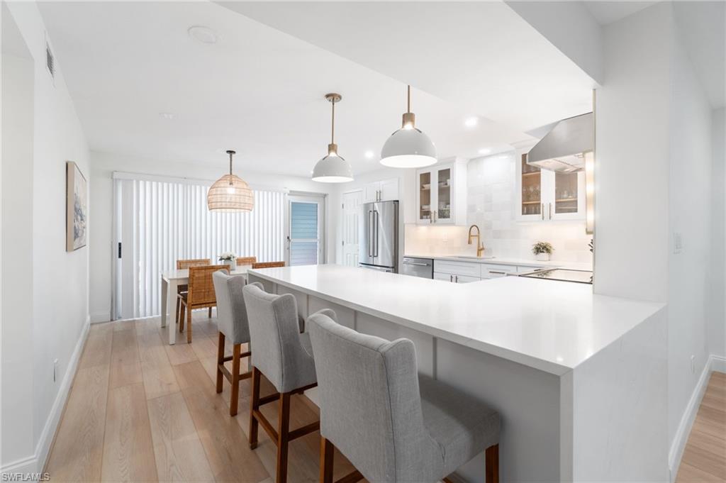 Kitchen with glass insert cabinets, a kitchen breakfast bar, a peninsula, pendant lighting, and light wood-type flooring