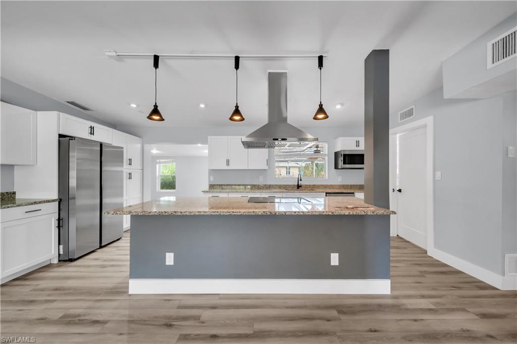 Kitchen featuring decorative light fixtures, island range hood, a kitchen island, stainless steel appliances, and white cabinets