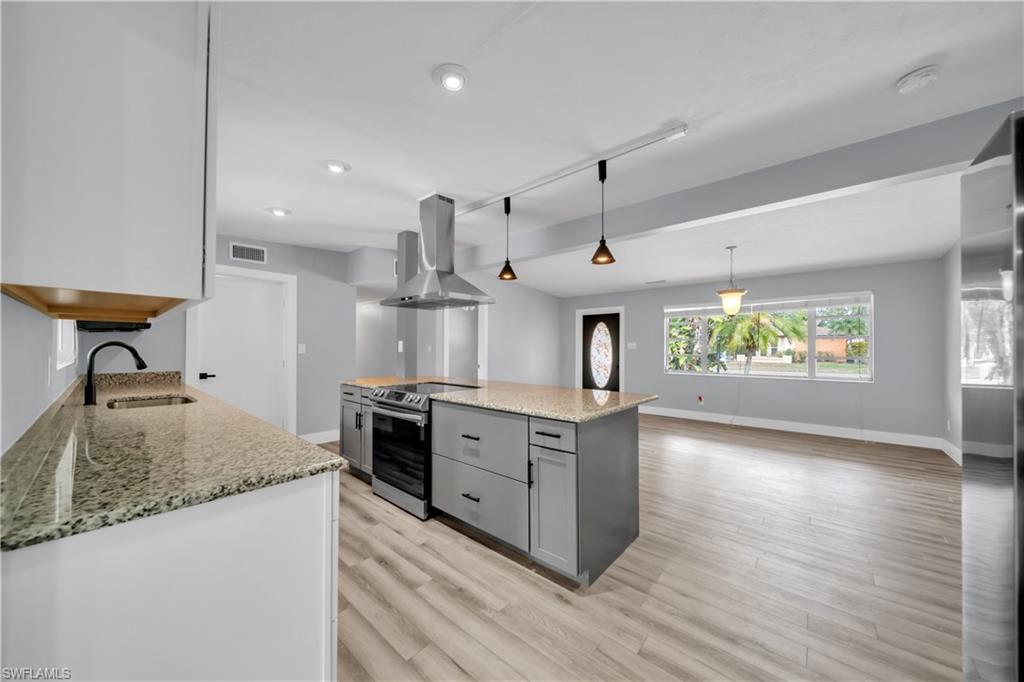 Two tone kitchen featuring light stone countertops, island range hood, stainless steel appliances, light wood-style flooring, and pendant lighting