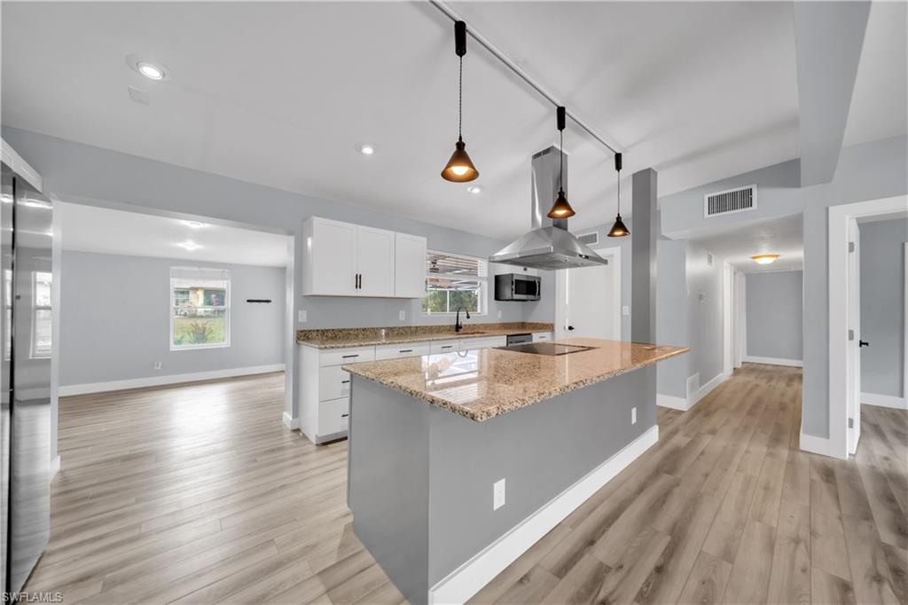 Kitchen featuring rail lighting, light stone counters, white cabinetry, island range hood, and a kitchen island