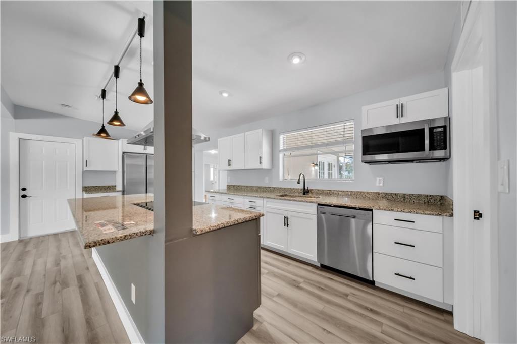 Kitchen with light stone countertops, stainless steel appliances, pendant lighting, a center island, and light wood-type flooring