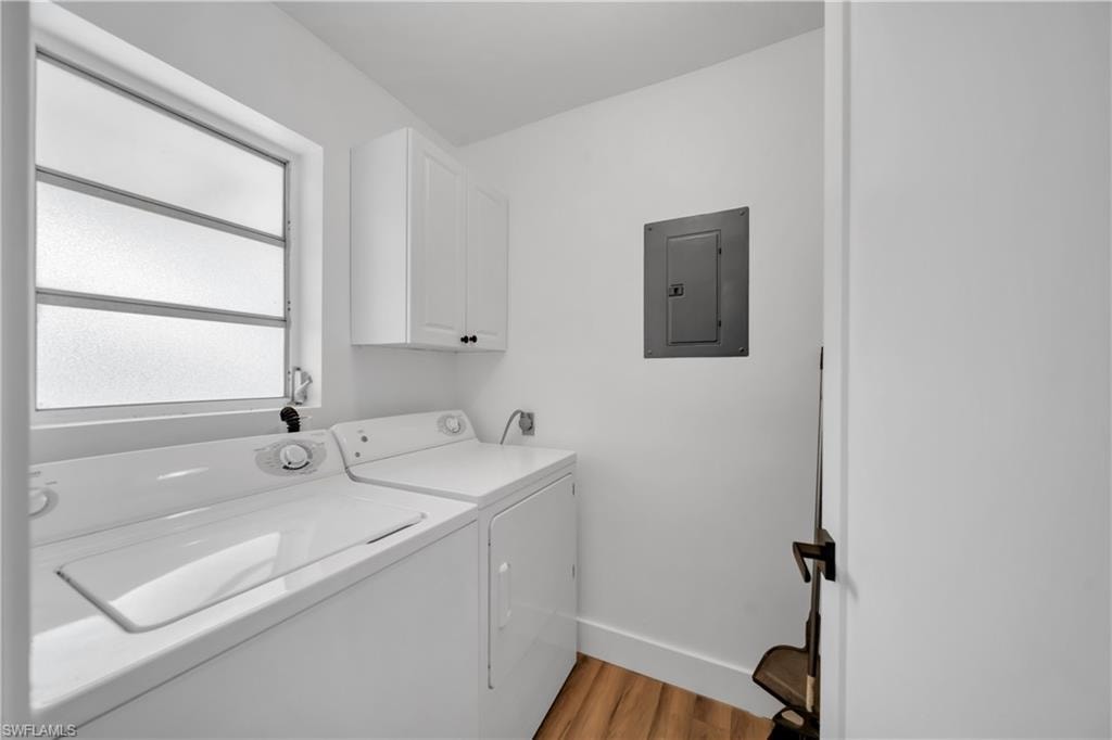 Laundry room featuring cabinet space, electric panel, light wood-style flooring, and separate washer and dryer