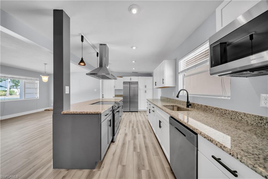 Kitchen featuring stainless steel appliances, light stone counters, island exhaust hood, dual tone cabinets, and decorative light fixtures