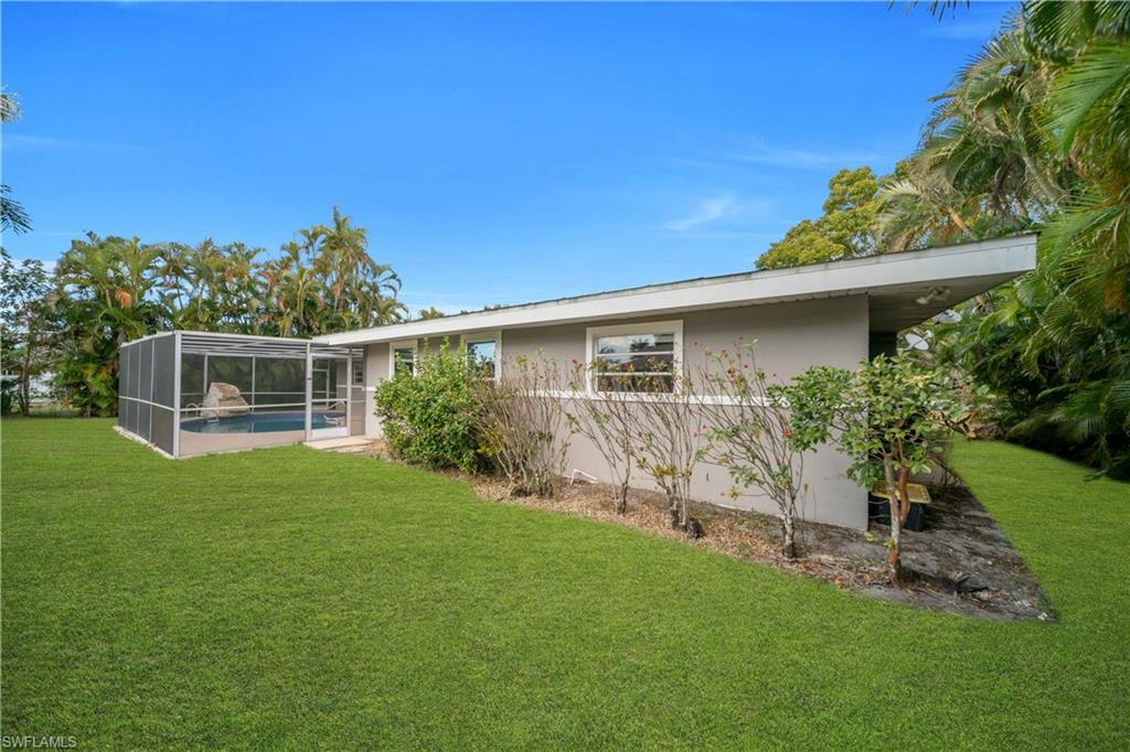 Rear view of property featuring a lawn, an outdoor pool, a lanai, stucco siding, and a sunroom