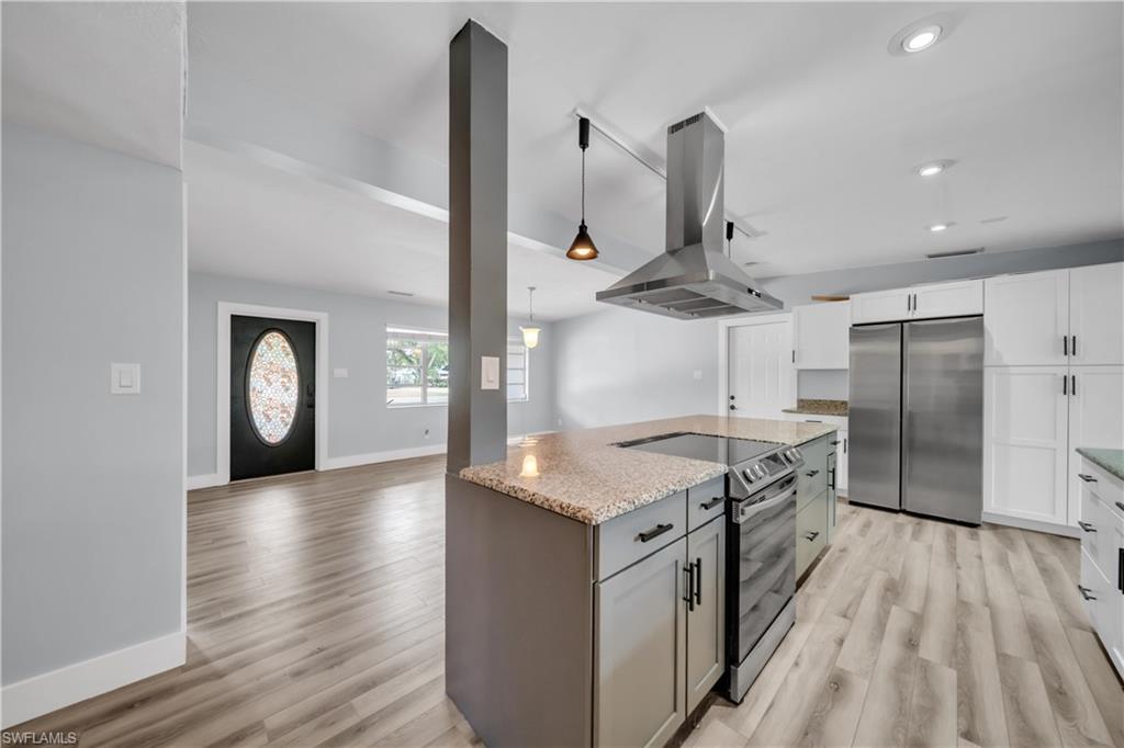 Dual tone kitchen featuring two tone cabinetry, island range hood, stainless steel appliances, light stone counters, and decorative light fixtures