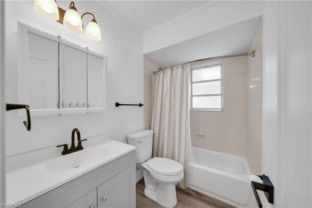 Bathroom with vanity, shower / bath combination with curtain, ornamental molding, and light wood-style flooring