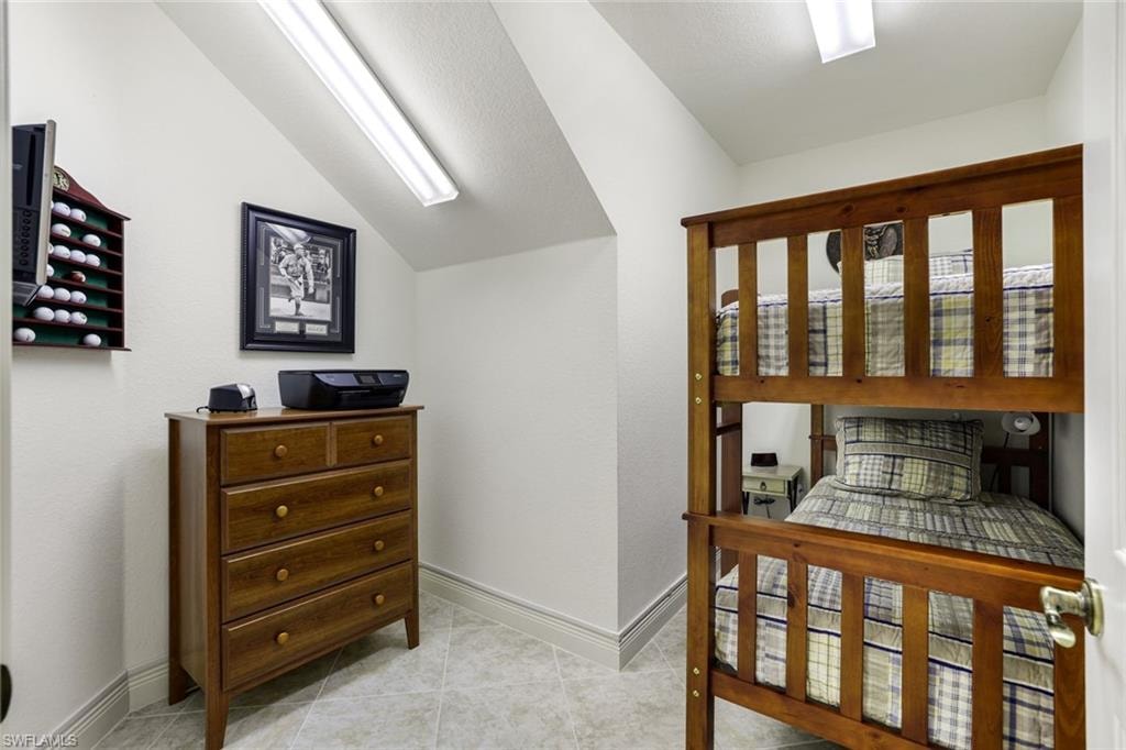 Bedroom with lofted ceiling, light tile patterned floors, and a textured wall