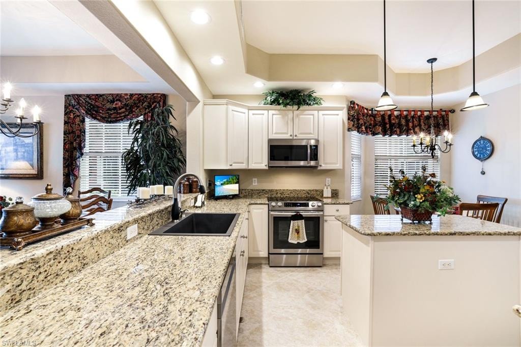Kitchen with hanging lights, stainless steel appliances, light stone counters, a center island, and white cabinetry