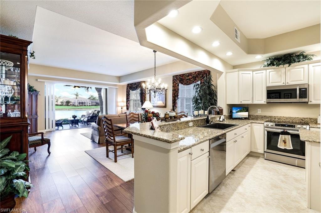 Kitchen with light stone countertops, stainless steel appliances, a peninsula, and white cabinetry