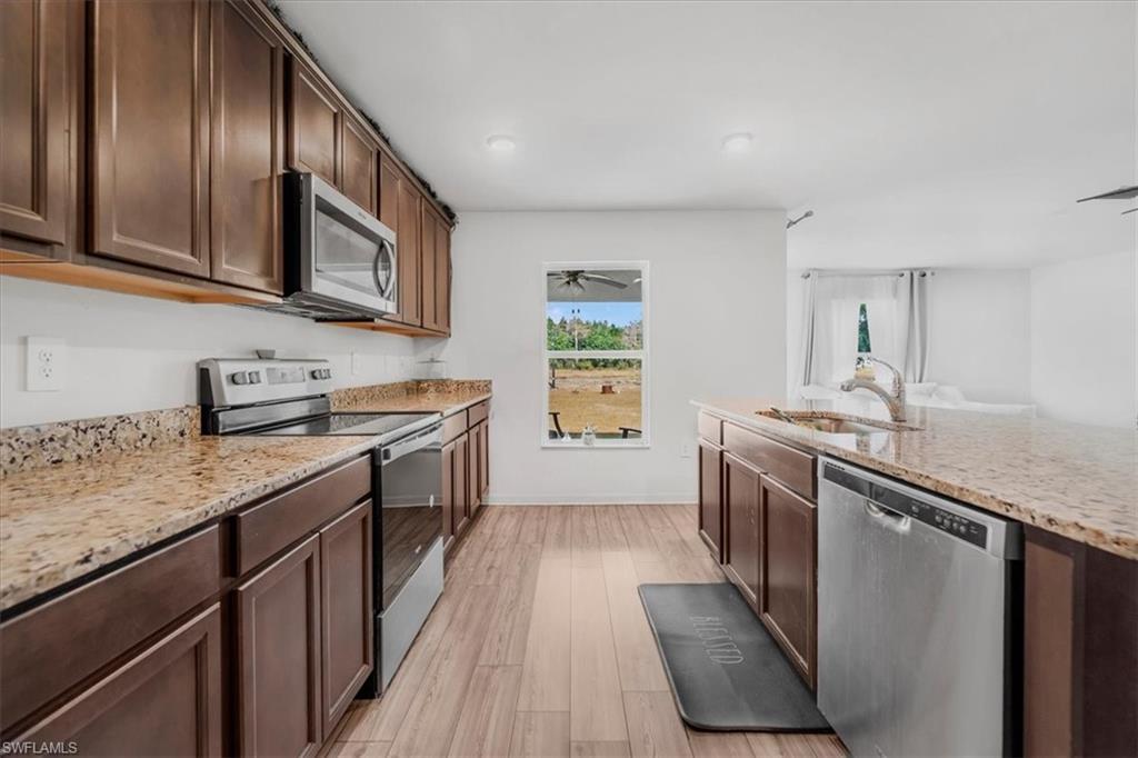 Kitchen featuring stainless steel appliances, light stone counters, light wood-type flooring, dark wood finish cabinetry, and open floor plan