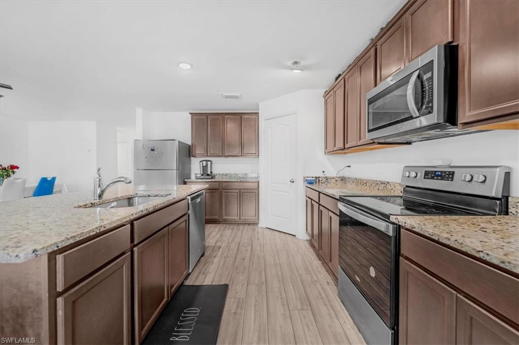 Kitchen with stainless steel appliances, light wood-style floors, light stone countertops, and an island with sink