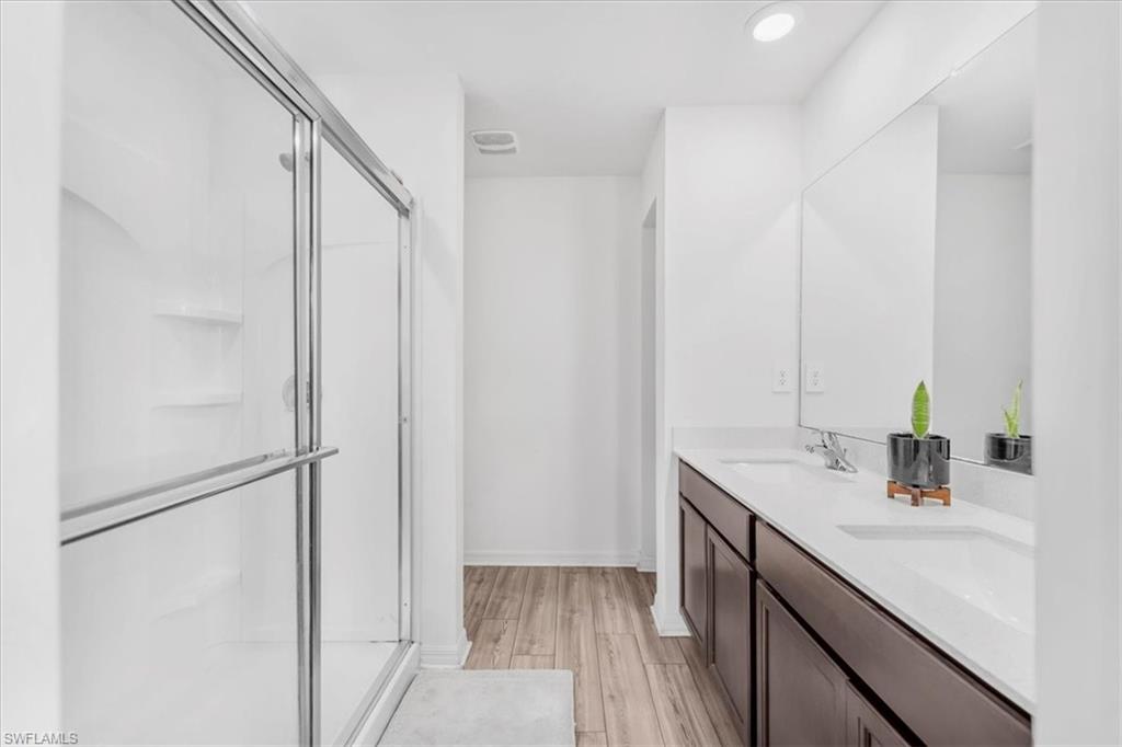 Full bath featuring a shower stall, double vanity, light wood-style floors, and recessed lighting