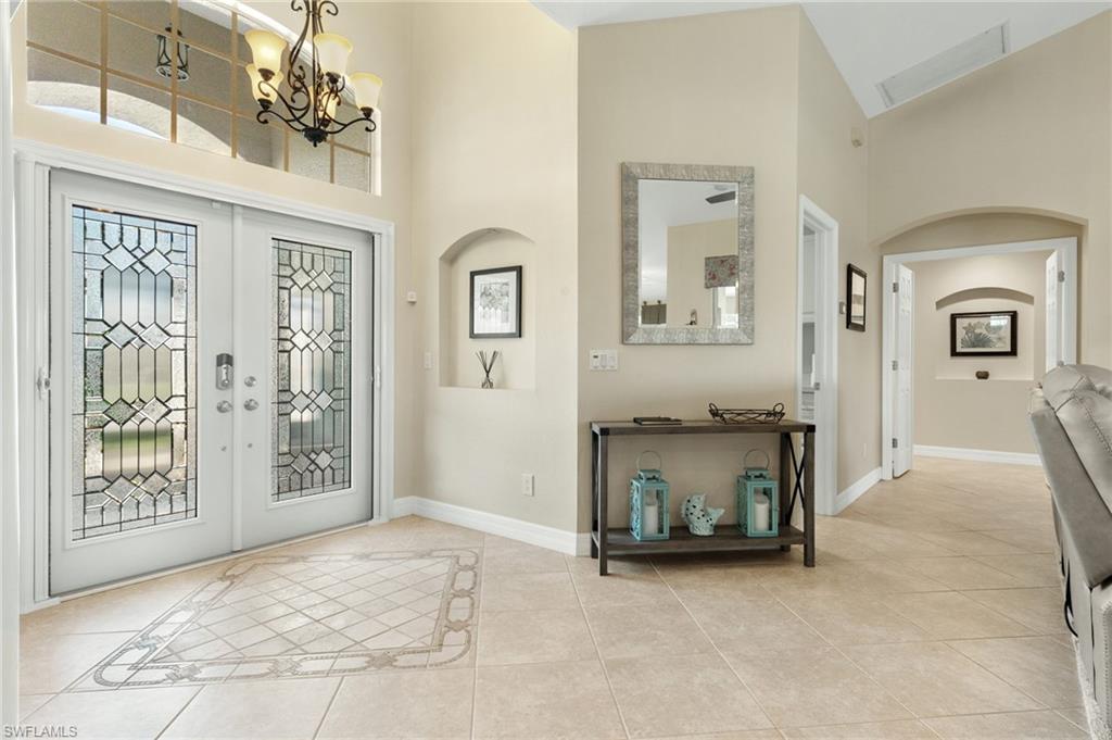 Entryway with french doors, light tile patterned floors, a chandelier, arched walkways, and inlaid floor details