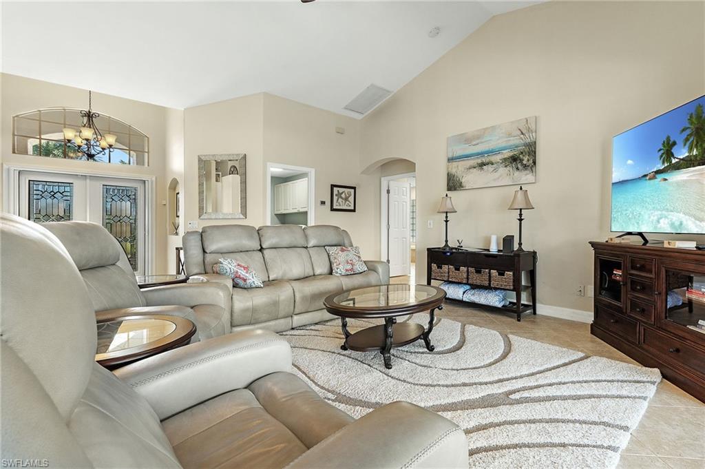 Living room with arched walkways, vaulted ceiling, hanging lights, light tile patterned floors, and french doors