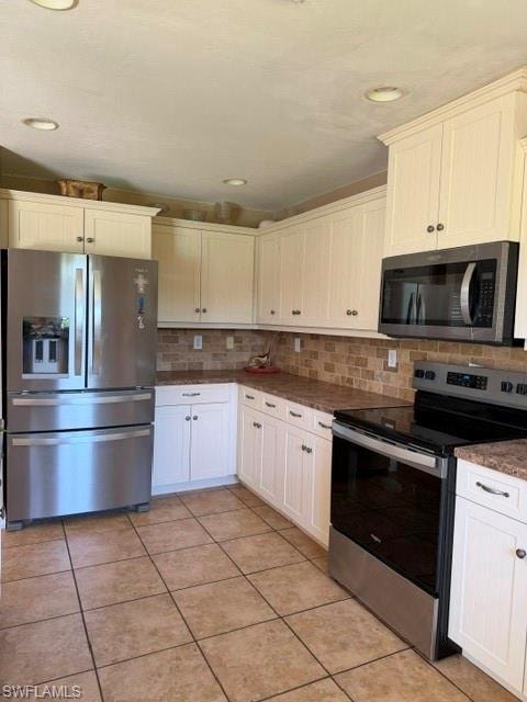 Kitchen with stainless steel appliances, decorative backsplash, white cabinetry, light tile patterned flooring, and dark stone countertops