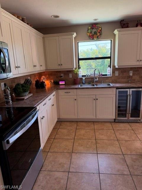 Kitchen with stainless steel range, beverage cooler, tasteful backsplash, light tile patterned flooring, and white cabinets