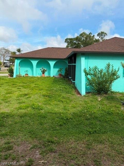 View of home's exterior with stucco siding, a lawn, and roof with shingles