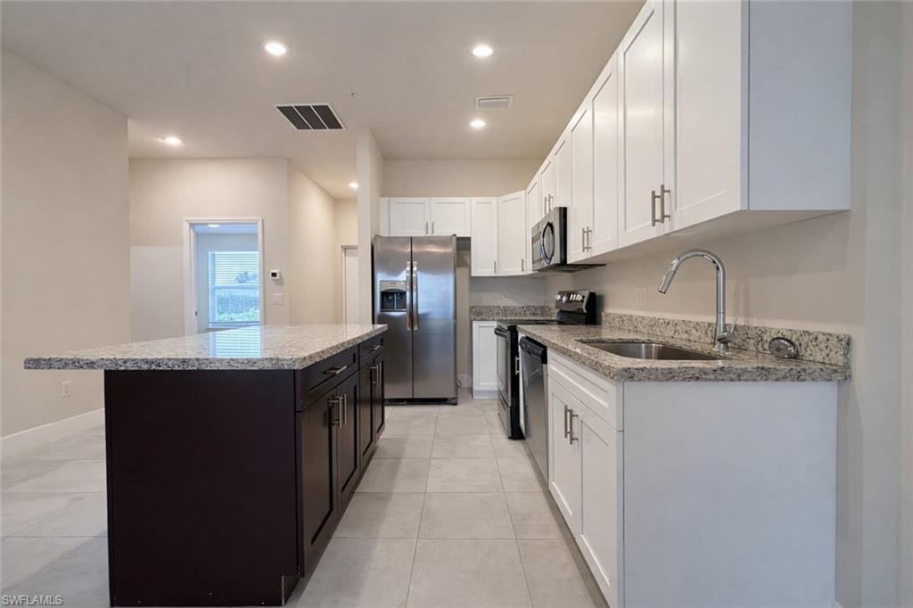 Kitchen with stainless steel appliances, a kitchen island, recessed lighting, ceiling fan, and light stone counters